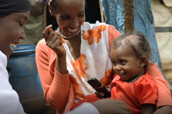 A mother holing her child on her arm while a health worker takes care of the child.